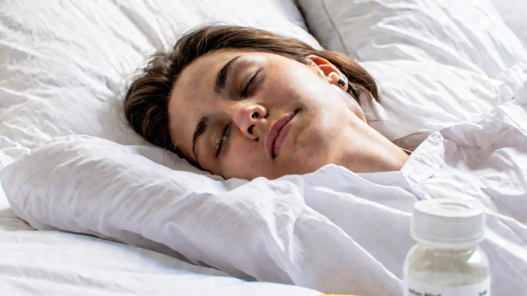 A young woman resting peacefully in bed with a medication bottle on the bedside table, symbolizing the importance of addressing sleep health and exploring treatment options for Obstructive Sleep Apnea (OSA), a condition characterized by interruptions in breathing during sleep.